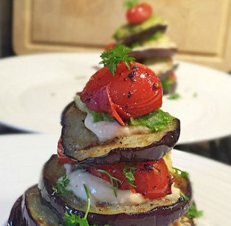 Een kleurrijk stapeltje gegrilde aubergine met avocado, hummus en tomaatjes