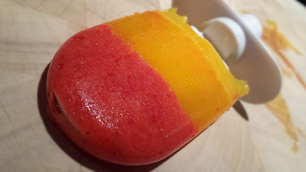 Gezond en kleurrijk zelfgemaakt raketijsje van aardbei, mango en sinaasappel